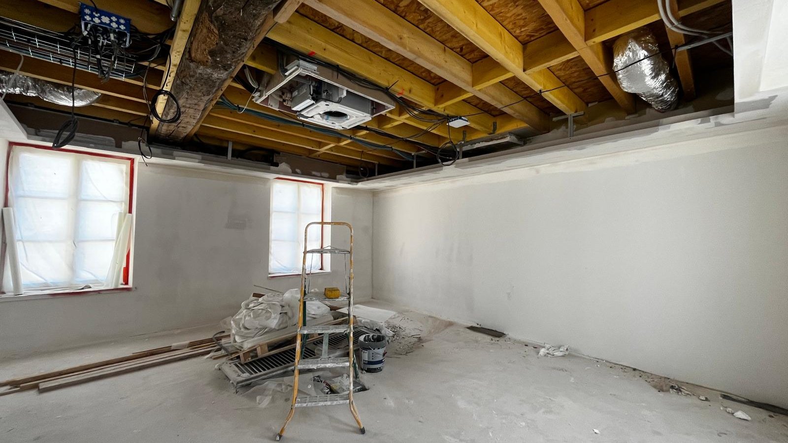 La salle de réunion avant travaux : plafond ouvert sur les solives et les gaines, murs enduits et fenêtres protégées
