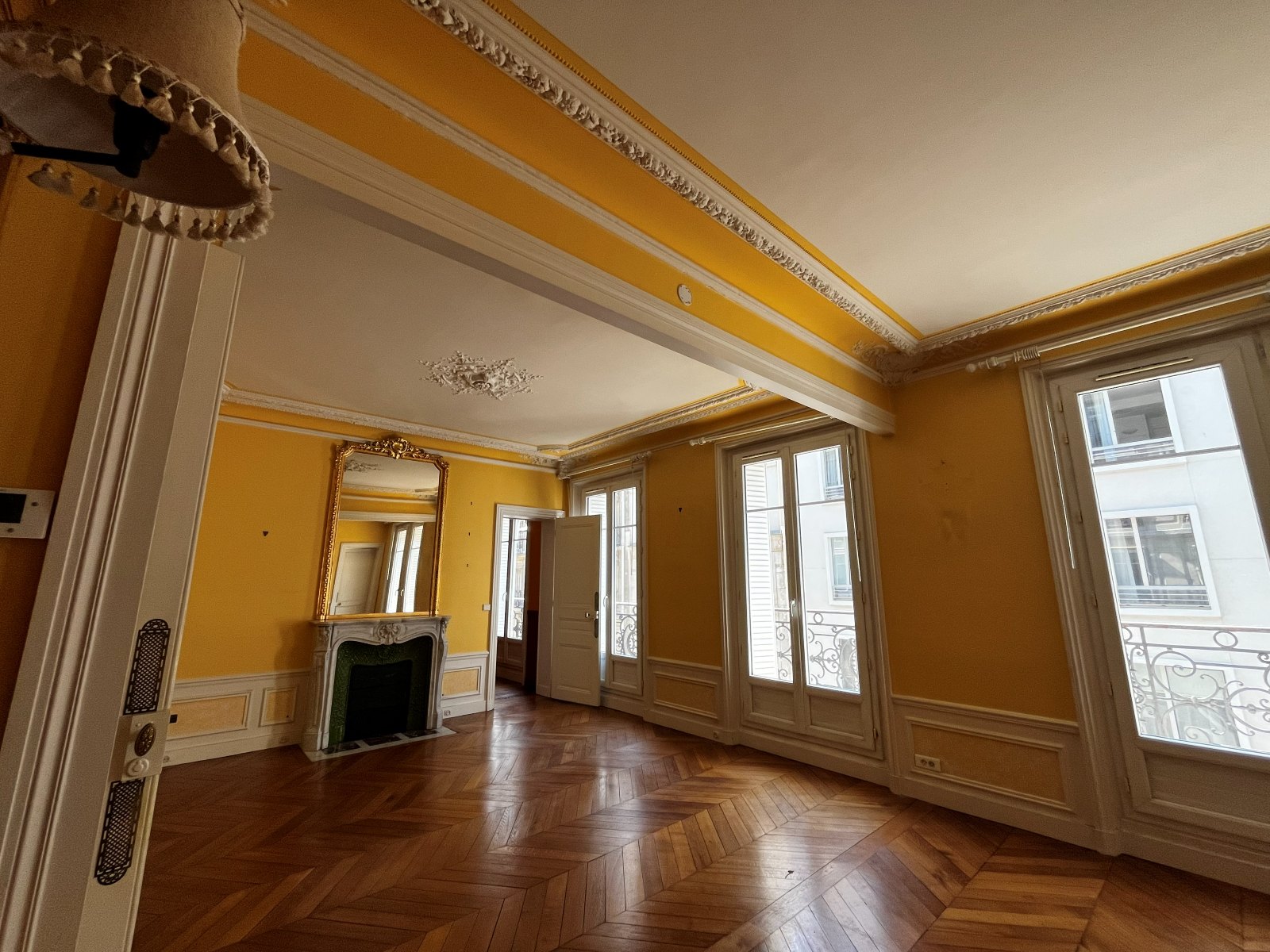 La pièce avant travaux : murs jaunes, moulures d'origine, cheminée en marbre et parquet en point de Hongrie