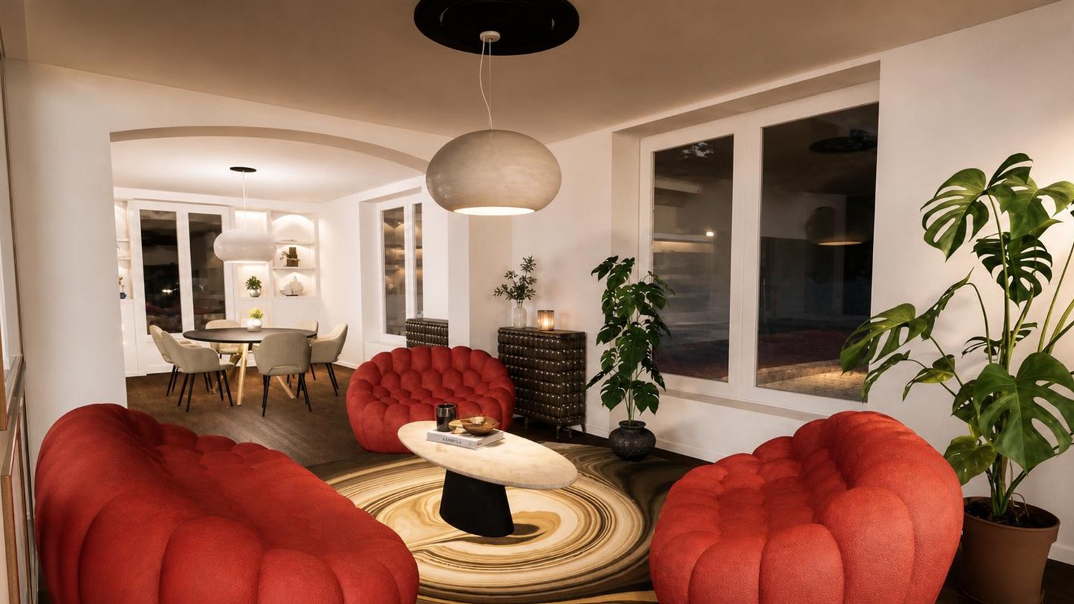 Salon le soir, fauteuils en velours rouge autour d'une table basse ovale et tapis à motif concentrique, ouverture sur la salle à manger
