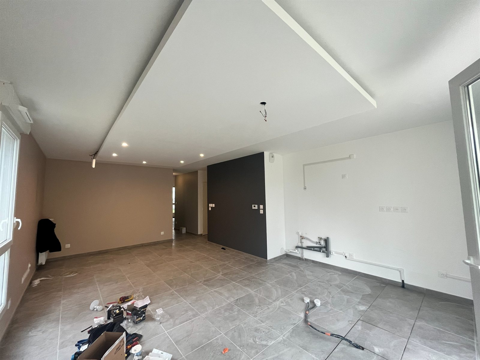 La pièce de vie avant travaux : faux plafond brut, murs nus, arrivées d'eau et câbles au sol